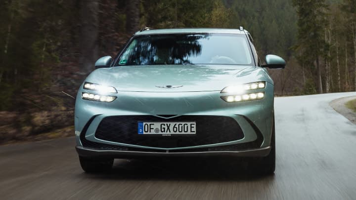 Blue Genesis GV60 driving down a wet road in woodland