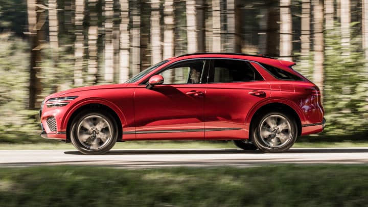 Red Genesis GV70 driving on a road with woodland either side