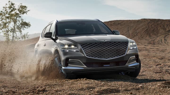 Grey Genesis GV8 driving in the dessert and kicking up sand