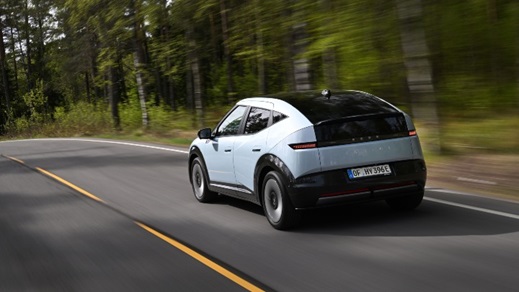 Light blue Hyundai IONIQ 3 driving through forest road, rear three-quarter view