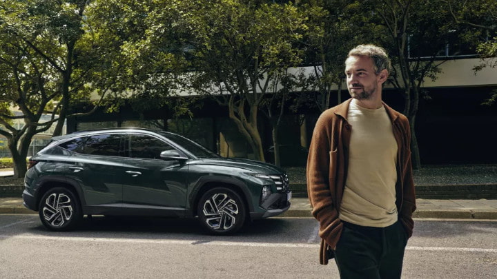 Side Of Green Hyundai TUCSON Parked On Road With Man in the Foreground
