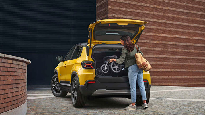 Woman loading a pram into the boot of a yellow Jeep Avenger