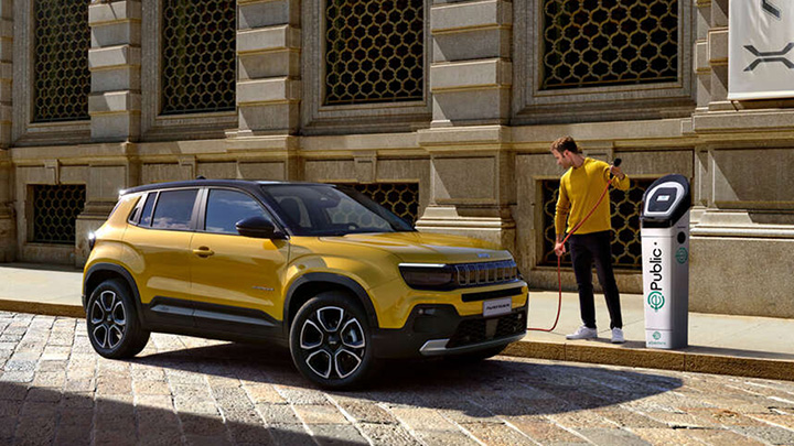 Man standing next to a yellow Jeep Avenger whilst it's parked up and charging