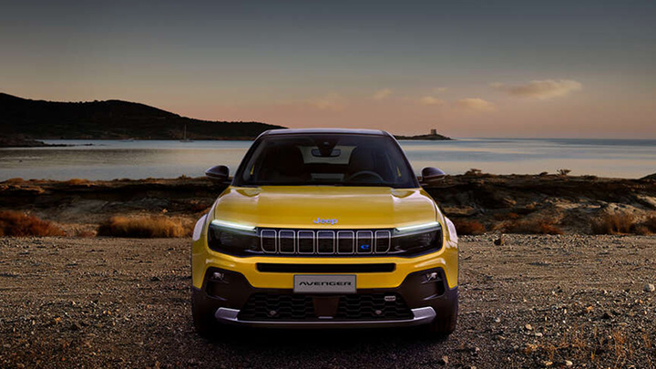 Front end shot of a yellow Jeep Avenger parked in front of a lake at sunset