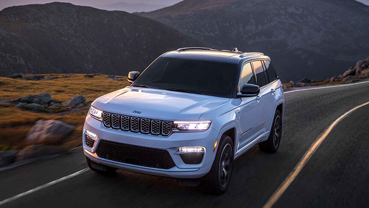 White Jeep Grand Cherokee driving on a road through a mountain range