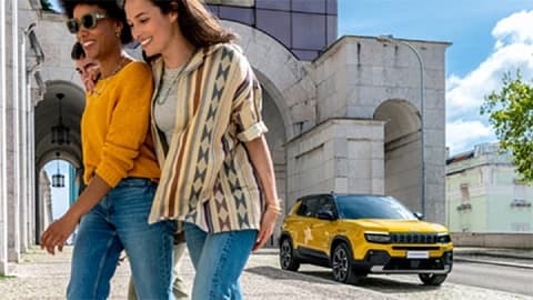 Two women walking away from a yellow Jeep Avenger, with a city background