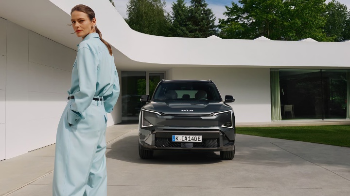 Grey Kia EV5 Exterior Front with Woman Outside Contemporary Home