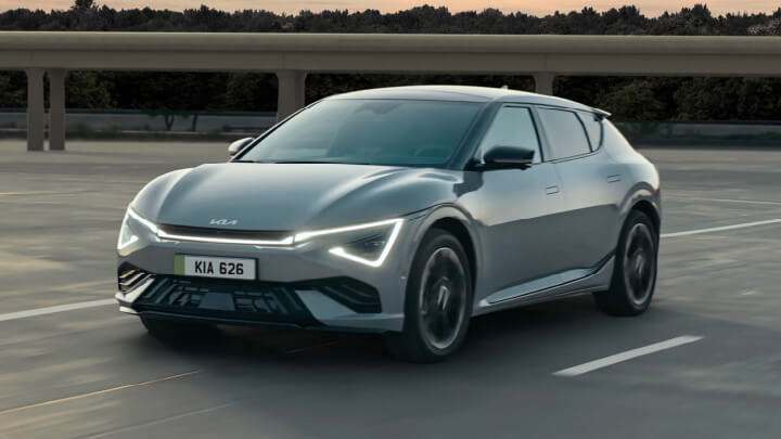 Silver Kia EV6 parked in a car park with a bridge and trees in the background