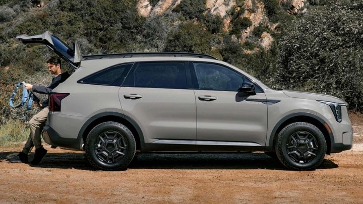 Side view of a silver Kia Sorento parked in the woods with the boot open and a man sitting on it