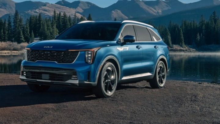 Blue Kia Sorento Hybrid parked in front of a lake with pine trees in the background