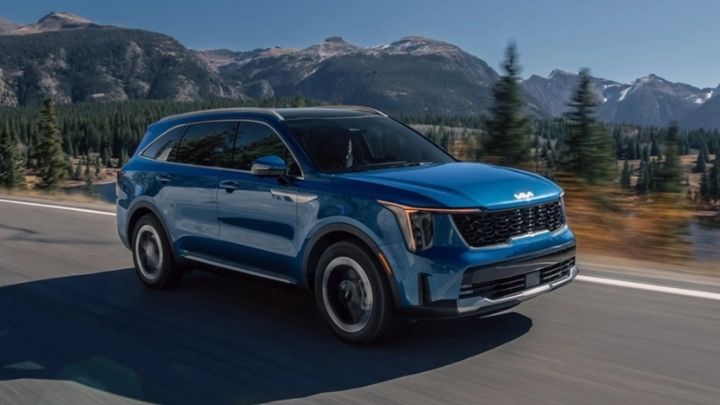 Blue Kia Sorento Hybrid driving in a motorway with a lake and pine tress to its left side