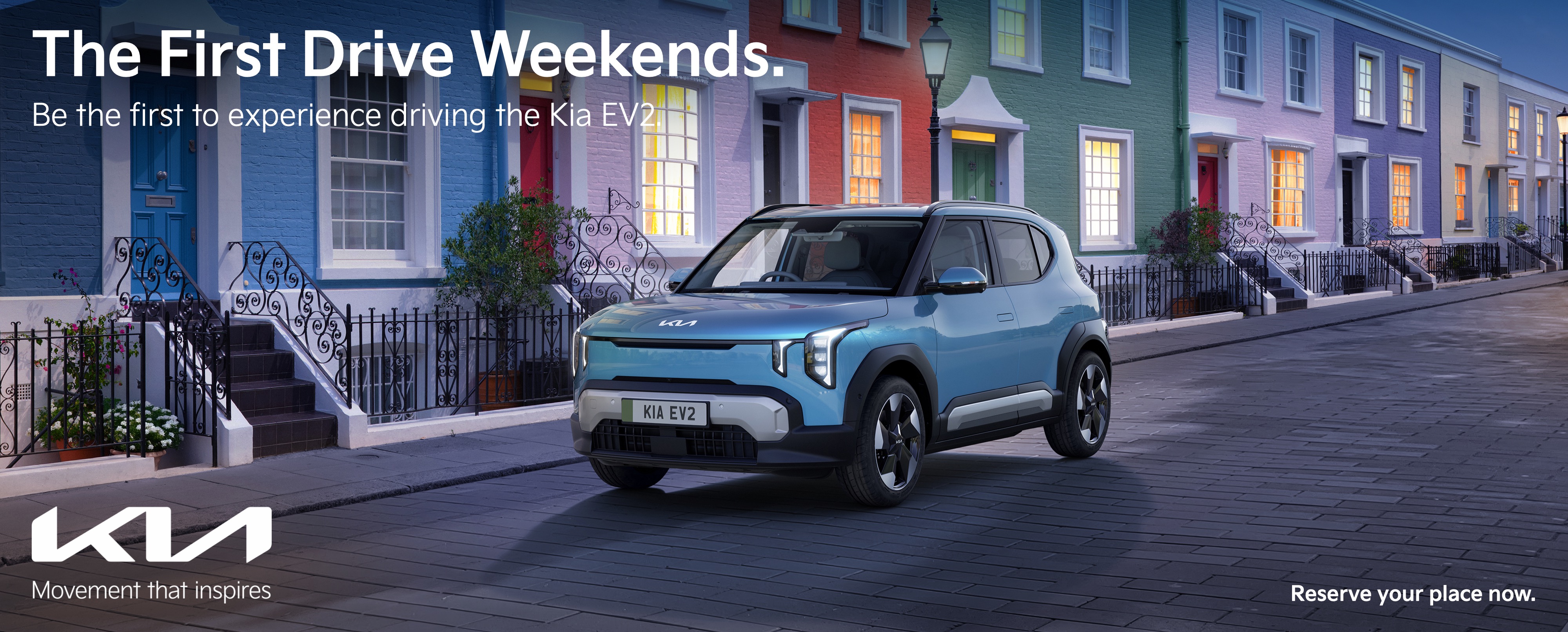 Blue Kia EV2 Driving Next To Terraced Houses