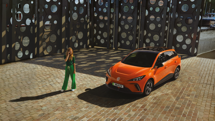 Woman Standing Infront Of Orange MG4 EV Front Shot
