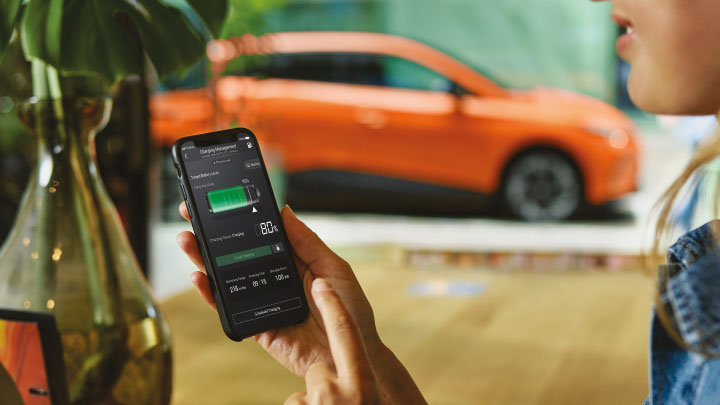 Woman Looking at Phone In Front of Orange MG4 EV Looking at Charging Statistics