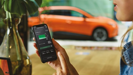 Woman Looking at Phone In Front of Orange MG4 EV Looking at Charging Statistics