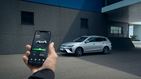 Man Looking at Phone In Front of Silver MG5 EV Looking at Charging Statistics