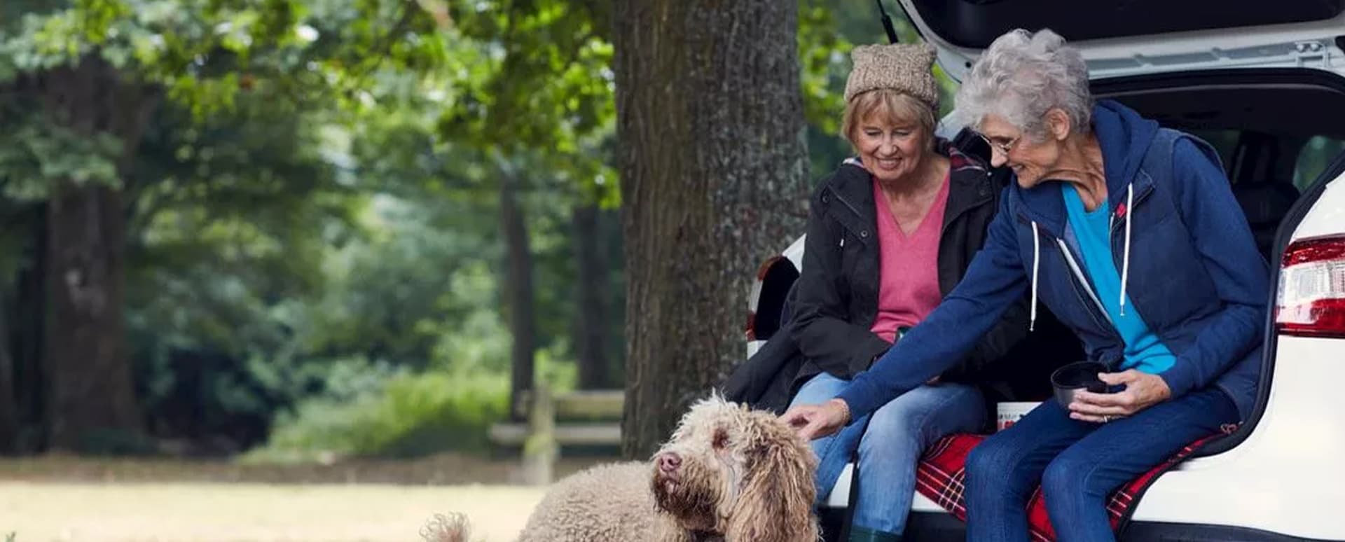 Two old ladies sitting in the open boot of a Nissan Qashqai in the countryside, whilst petting a dog