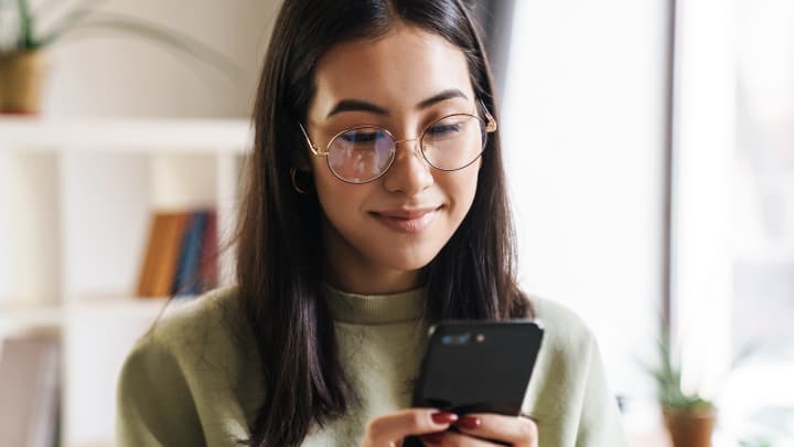 Dark haired woman typing on her smartphone whilst smiling