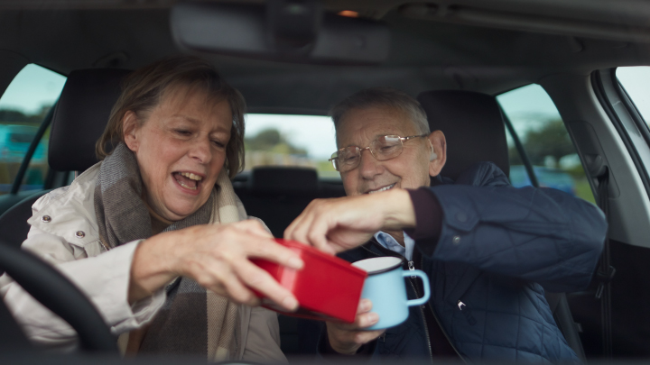 Two elderly people enjoying a tea and biscuit in the car