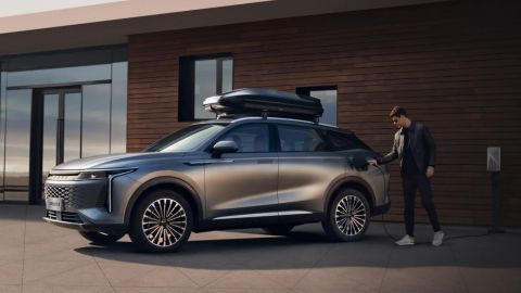 A man charging his OMODA vehicle that is parked in front of a modern looking house