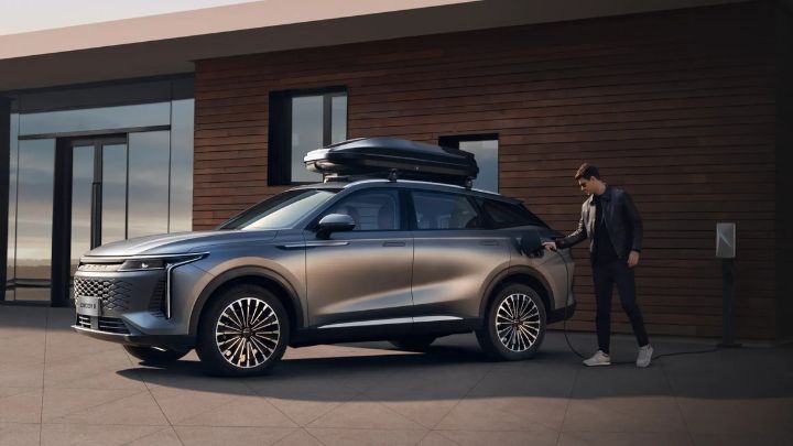 A man charging his OMODA vehicle that is parked in front of a modern looking house
