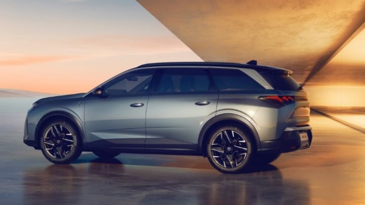 Side of a silver Peugeot 5008 parked in front of a orange wall and with a view to the sky