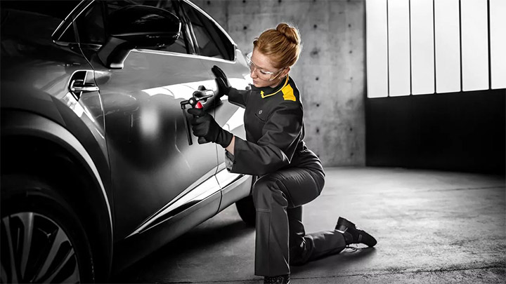 Woman in overalls working on the door of a grey Renault