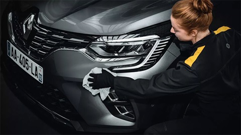 Young woman in overalls polishing the front bumper of a grey Renault Arkana