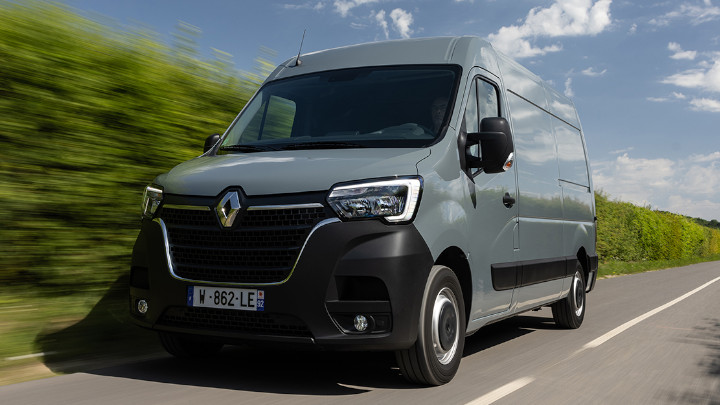 Front Exterior of a Grey Renault Master Van Driving Along a Road Lined by a Green Hedge