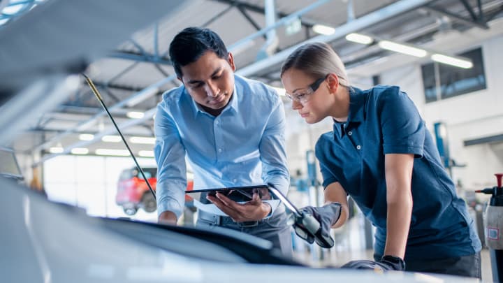 Two technicians looking under the bonnet of a car during a health check