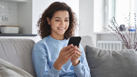 Young woman sitting on a sofa looking at her phone for a health check report